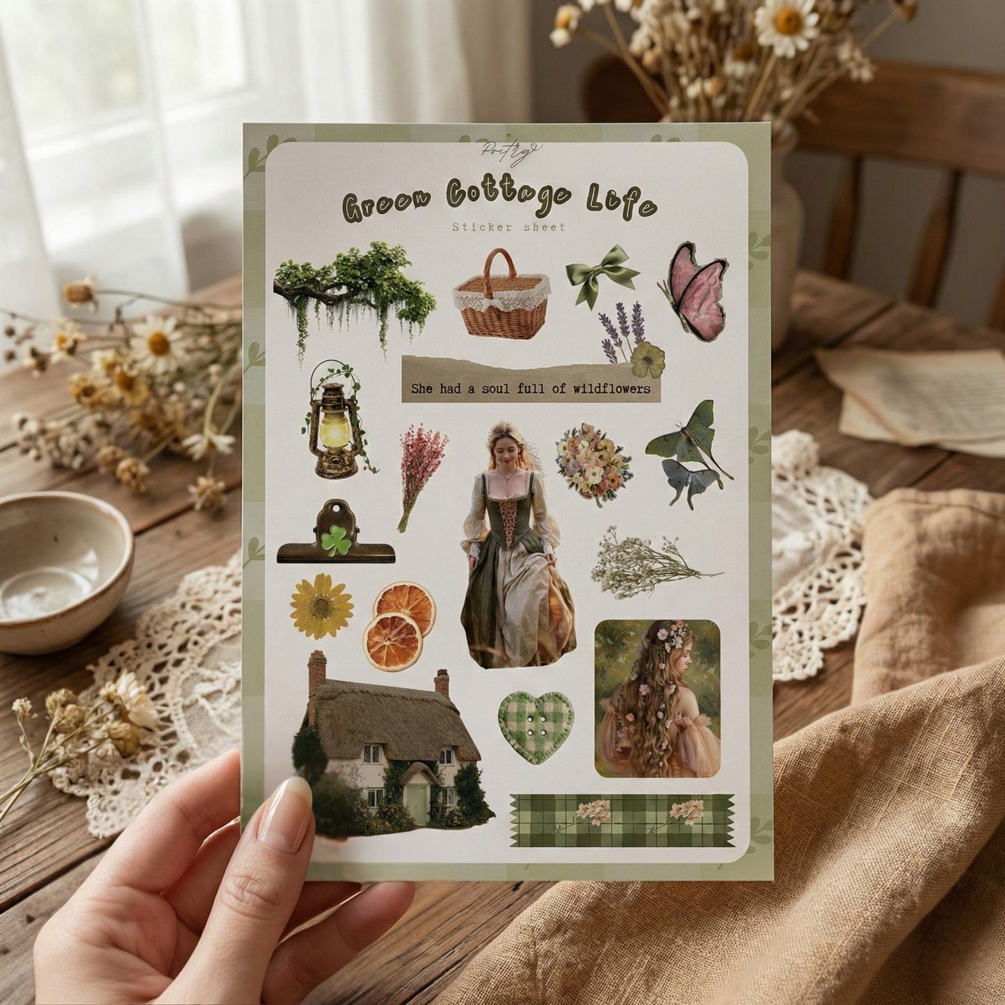 Sheet of 'Green Cottage Life' stickers held over a rustic wooden table with dried flowers.
