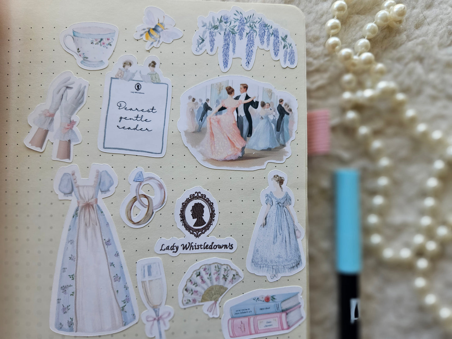 Sticker sheet with vintage-themed designs on a notebook with a pearl necklace in the background.