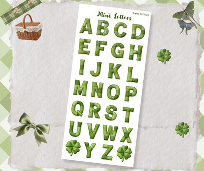 Sheet of green letter stickers on a textured surface with decorative elements.