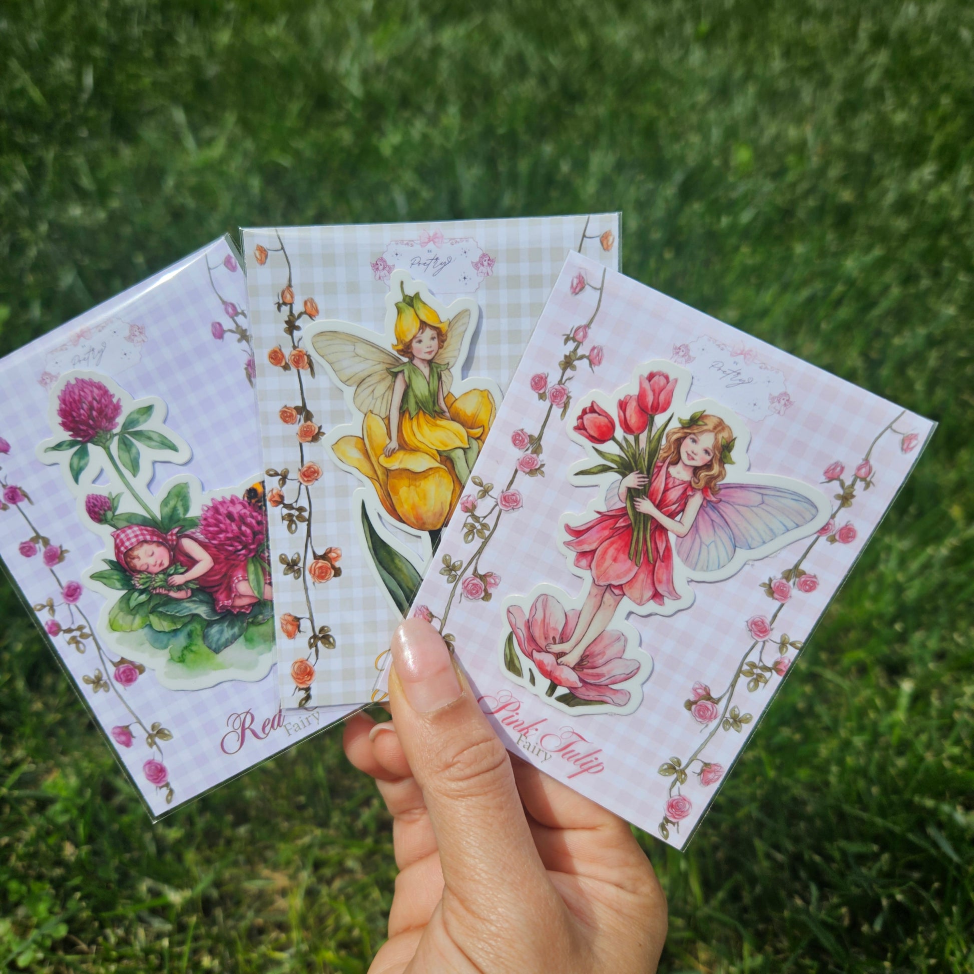 Hand holding three colorful fairy cards against a grassy background
